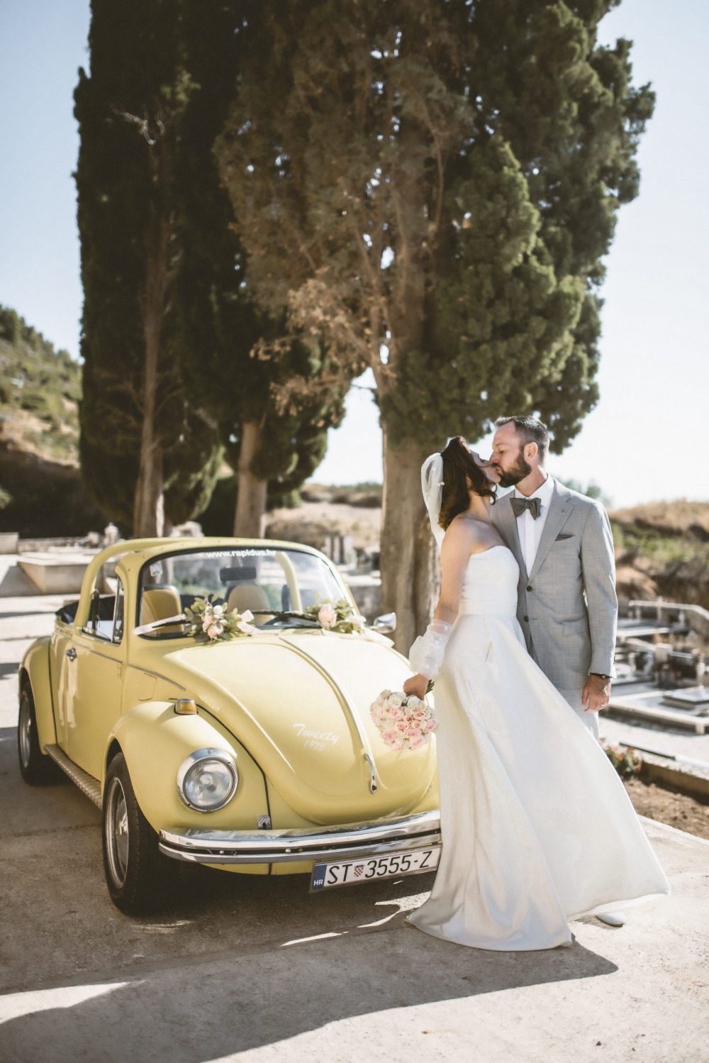 Newlyweds kissing by their vintage yellow Beetle car
